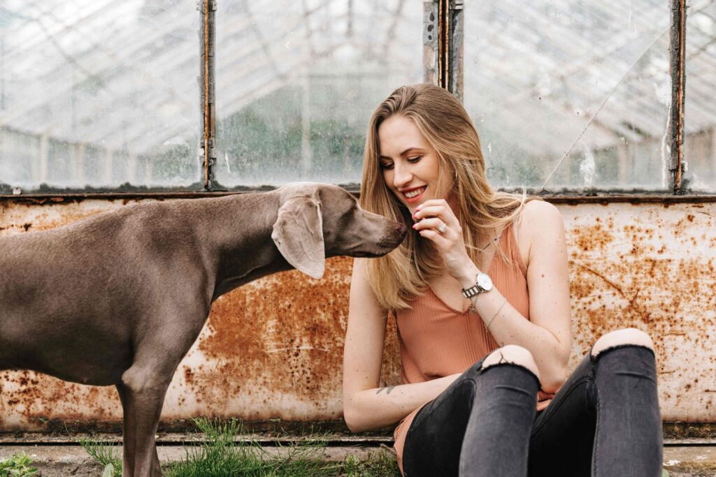 Woman sitting outdoors smiling as dog nuzzles her face
